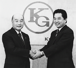 社長就任会見で谷脇会長とがっちり握手する宮﨑社長