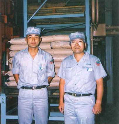 日本特殊塗料(株) 自動倉庫を前に松尾久雄製造課第一係と森幸夫製造課長